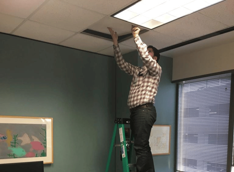 A guy standing on a ladder pushing a ceiling tile in